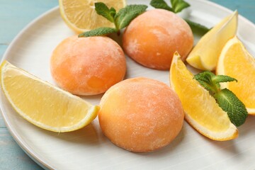 Plate with tasty mochi, cut orange, lemon and mint on light blue wooden table, closeup