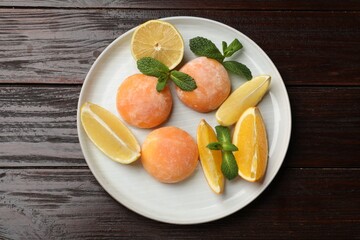 Plate with tasty mochi, cut orange, lemon and mint on wooden table, top view