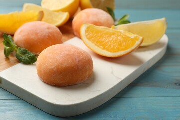 Board with tasty mochi, cut orange and mint on light blue wooden table, closeup