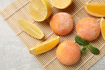 Bamboo mat with tasty mochi, cut orange, lemon and mint on grey textured table, flat lay