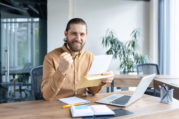 Successful businessman at his office desk celebrates by reading important documents and smiling. Captures the spirit of achievement, professional work environment, and modern business workplaces.