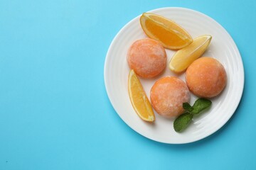 Plate with tasty mochi, cut orange and mint on light blue table, top view. Space for text