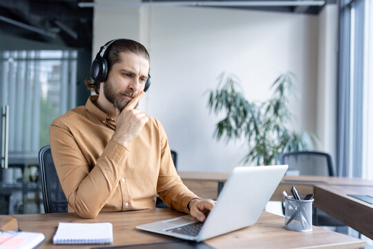 Professional individual wearing headphones focused on work using a laptop, seated in a contemporary office space.