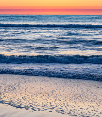Early morning sunrise illuminates the gentle waves on the sand in Corolla