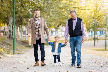 Obraz premium A father, a son and a grandfather have fun one day in a park in the afternoon.The family walks hand in hand in the park.Concept of intergenerational family.