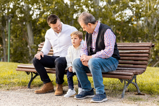 A father, a son and a grandfather have fun one day in a park in the afternoon.The family is sitting on a wooden bench while they chat.Concept of 3 generations of family.