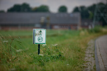 Bicycle path sign, number 61,  SES West-Brabant, pointing upwards. Rural roadside scene.