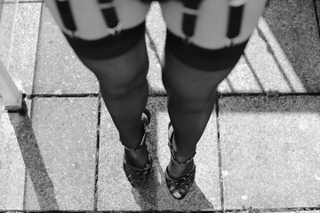 Fetisch Model mit schwarzen Nylons / Strapsstrümpfen mit Naht, Strapse und schwarzen Lack Plateau High-Heels steht auf einem Balkon