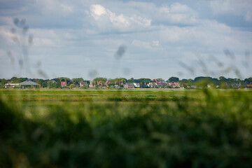 Fototapeta premium Low-lying, rural Dutch village nestled in a green field. Cloudy sky above.