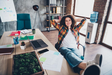 Young businesswoman with curly hair relaxing in modern office with casual style and checkered shirt