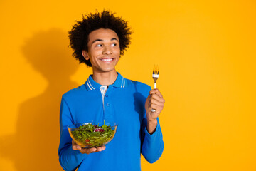 Portrait of nice young man fork salad look empty space wear blue shirt isolated on yellow color...