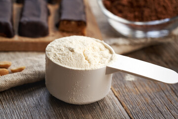 A scoop of whey protein powder with homemade healthy chocolate bars and raw cacao in the background