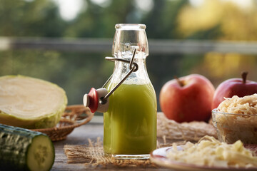 A bottle of green cabbage and cucumber juice with red apples and sauerkraut
