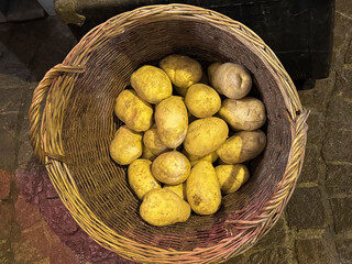 Wicker basket filled with fresh yellow potatoes on cobblestone street