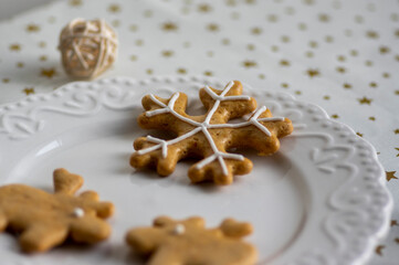 Painted traditional Christmas gingerbreads arranged on white plate, tablecloth with golden stars, snowflake and reindeer shapes