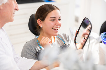 During appointment, dentist demonstrates to patient result of cosmetic dental filling. Senior man...