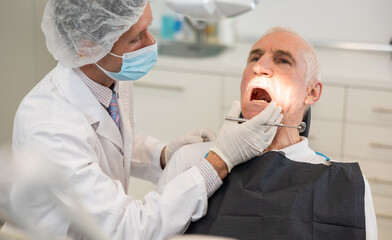 Mature man is sitting in armchair during dental diagnosis at dentist appointment. Male doctor...