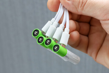 Four rechargeable batteries with plugged in USB plug charging wires in hand, close-up, Textured surface