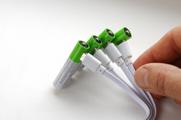 Four rechargeable batteries with plugged in USB plug charging wires in hand, close-up on white background