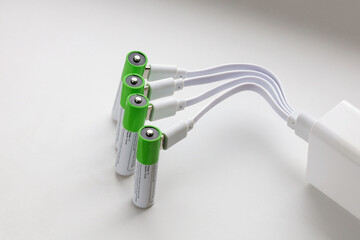 Four rechargeable batteries with plugged in USB plug charging wires in power adapter, close-up on...