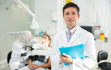Male doctor dentist with documents standing in dental office, clinic employee in suit uniform near...