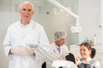 Obraz premium Senior man dentist doctor in white coat cooperates with clinic, works as general practitioner in dental department of clinic. Doctor enjoys working in profession.