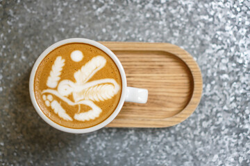 A cup of latte coffee with art cream foam in a white ceramic cup on a wooden tray. 