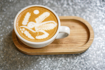 A cup of latte coffee with art cream foam in a white ceramic cup on a wooden tray. 