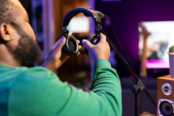 Trained audio technician picking up his headset for a recording session, mixing and mastering his...