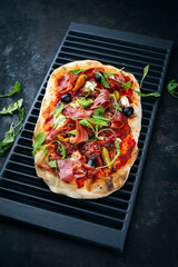 Traditional Italian pinsa bread prosciutto e salsa di pomodoro with Parma ham, buffalo mozzarella tomato sauce served as close-up on an old rustic grill grid