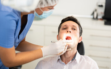 Man is sitting in armchair during dental diagnosis at dentist appointment. Girl doctor conducts...