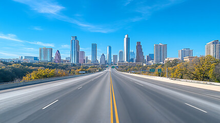 Fototapeta premium Empty highway leading towards modern city skyline under a bright blue sky