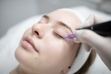 A woman relaxes during a beauty procedure focused on permanent makeup application in a salon. The...