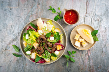 Mixed green leafy summer salad with Japanese soba buckwheat noodle, honeydew melon and peppermint served as top view with sweet sour chili dressing in a design plate