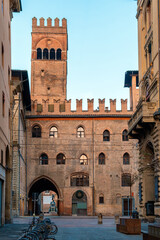 Fototapeta premium Narrow street in Bologna old town, Emilia Romagna, Italy, featuring historic architecture and the iconic Palazzo del Podesta at sunrise with nobody. Vertical orientation. Travel destination in Europe