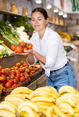 Portrait of positive satisfied girl buying fresh tomatoes in grocery shop