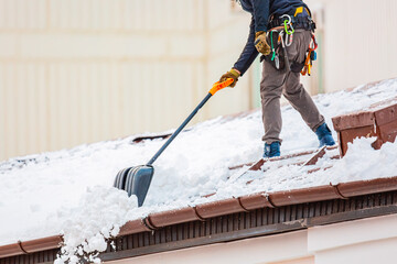 Communal services worker industrial climber removes snow from the building roof in winter. Cleaning...