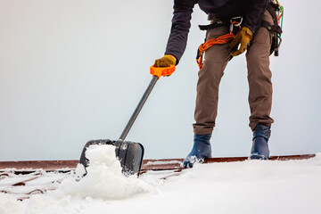 Communal services worker industrial climber removes snow from the building roof in winter. Cleaning...