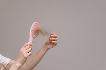 Hands holding a pink hairbrush with a clump of hair, against a plain background. Concept of hair loss, shedding, and hair care concerns.