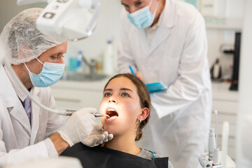 Girl sit in armchair during visit to male dentist and undergoes diagnostic procedure. Doctor...