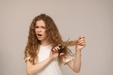 A woman with curly hair cutting her own hair with scissors, displaying a distressed and emotional...