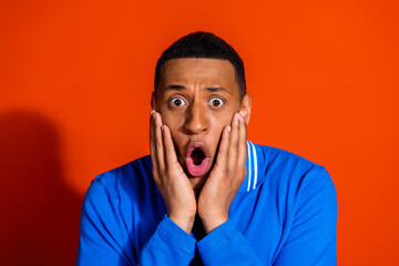 Surprised young man in blue shirt with orange background expressing astonishment