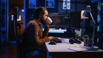 Focused programmer drinking coffee in apartment while solving database errors on computer. Remotely...