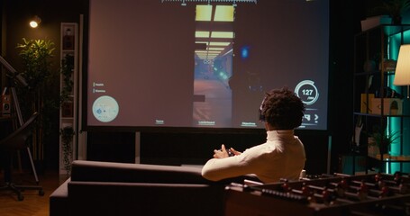 African american man playing shooter videogame on ultrawide TV with gun shooting laser bullets at flying robots. Panning shot of gamer enjoying competitive PvP fps internet multiplayer tournament game