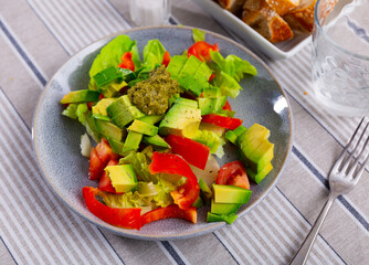 Plate contains portion of salad of fresh seasonal vegetables, complemented by small carafe of olive oil. Salad made from bell pepper, chin cabbage, avocado, pesto dressing