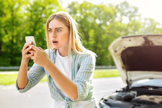 Terrified blonde woman looking for signal after car breakdown, holding smartphone, cannot find mobile network, having difficulty calling roadside assistance. Road problems concept