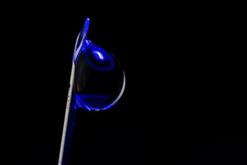Macrophotography of a drop of water attached to the tip of the syringe needle.with blue light...