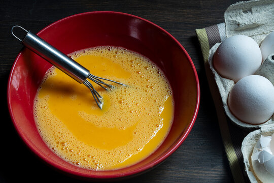 Whisking eggs. Whipped raw eggs in a red bowl with whisk for omelet , closeup. Breakfast preparation, rustic style
