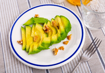 Appetizing ripe avocado slices served with walnuts to table..