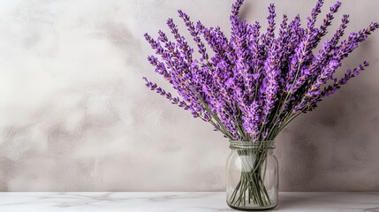 Bouquet of lavender flowers in glass jar on marble table against grey wall